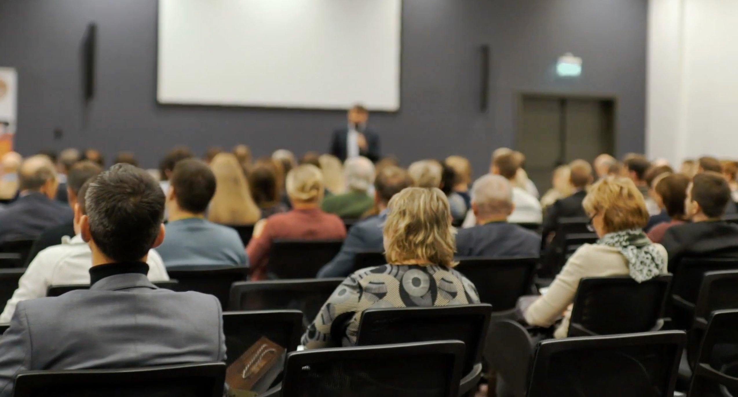 Photo of students in a lecture hall with a professor at the front of the class