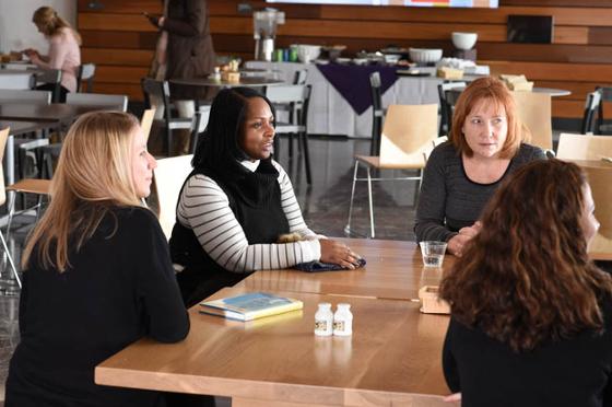 Photo of a group of four Chatham University instructors, seated at a table indoors at Eden Hall Campus