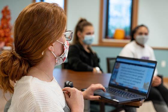 Photo of students wearing masks, sitting around a room